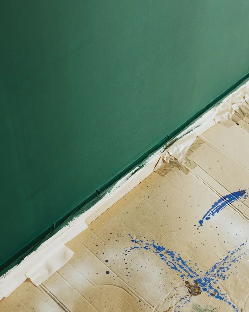 Frisch dunkelgrün gestrichene Wand, der Boden davor mit Pappe abgedeckt
