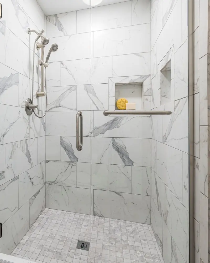 Geflieste Dusche mit Glastür, Wandfliesen in Marmoroptik, Ablagenische und Mosaikboden