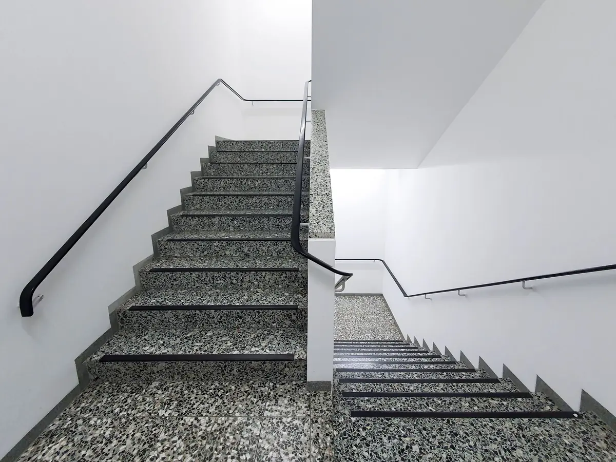 Helles Treppenhaus mit Terrazzostufen und schwarzen Handläufen