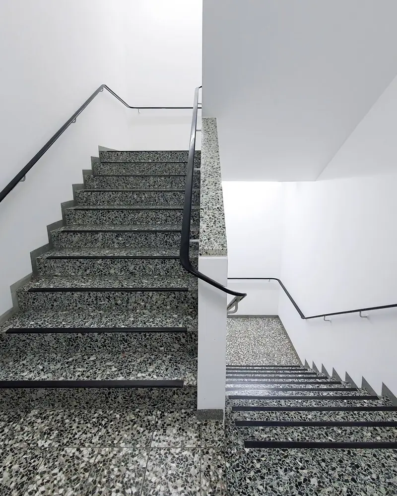 Helles Treppenhaus mit Terrazzostufen und schwarzen Handläufen