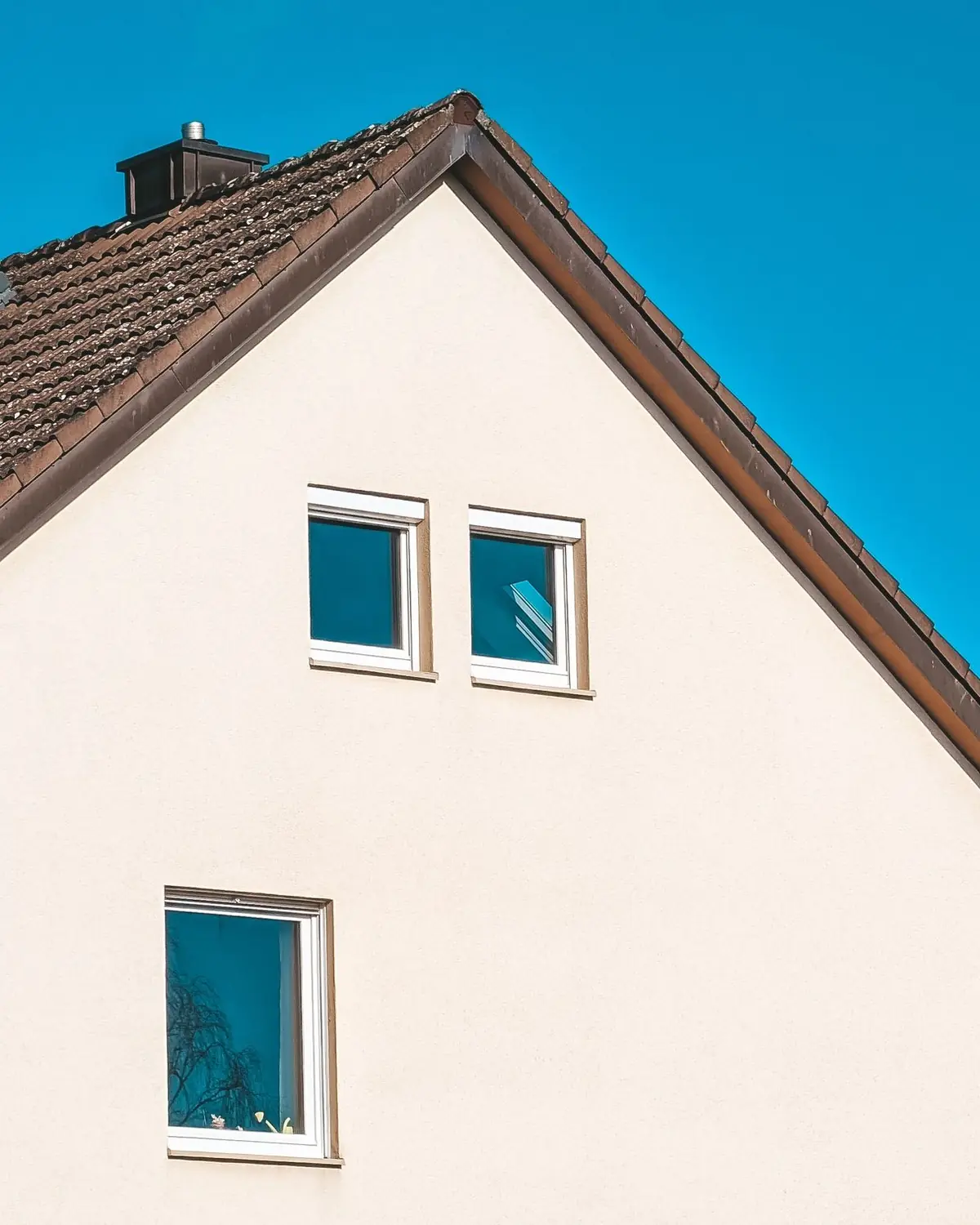 Giebel eines Einfamilienhauses mit hell verputzter Fassade, neuen Kunststofffenstern und Dachflächenfenstern vor blauem Himmel