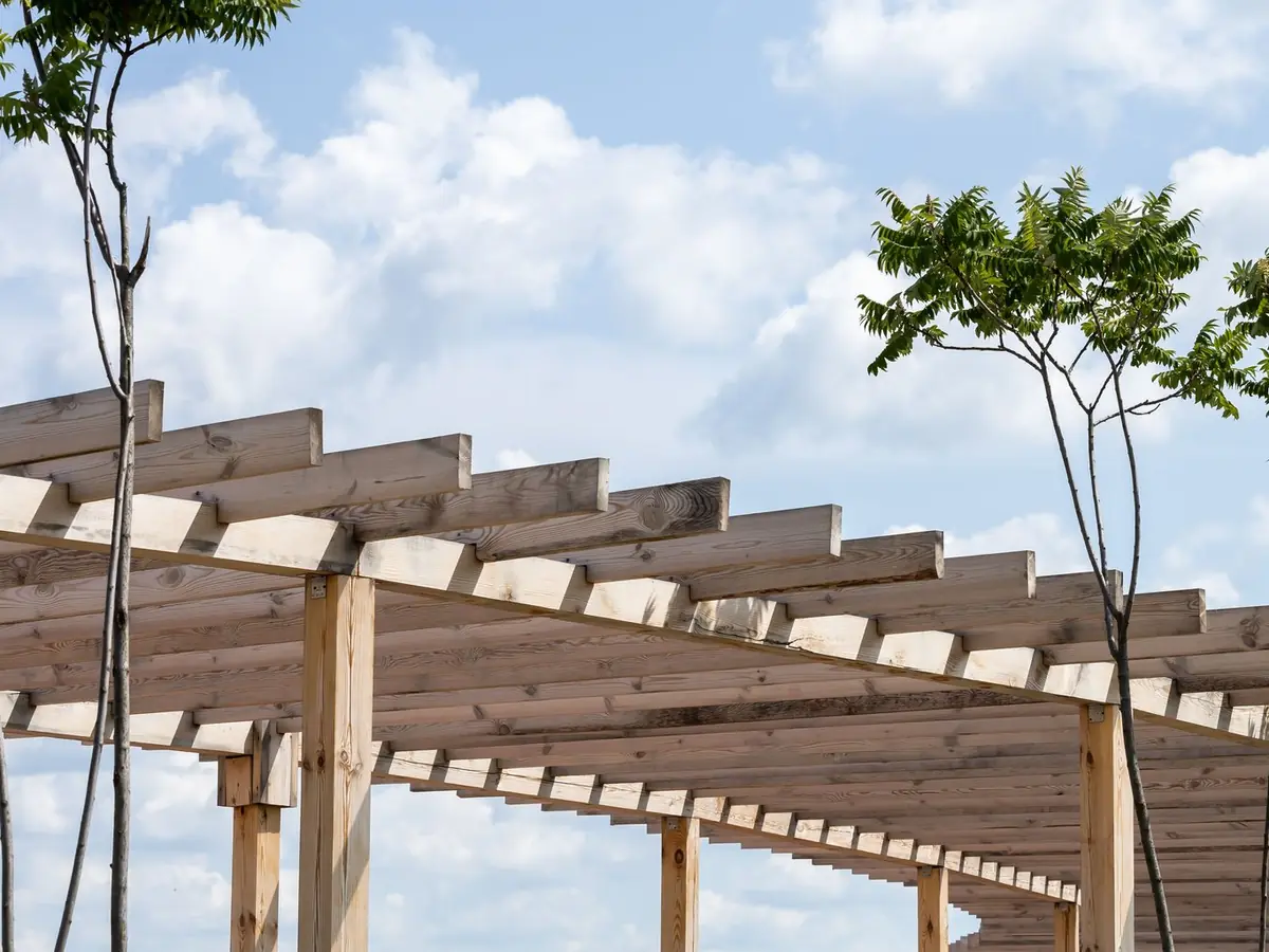Lange Pergola aus unbehandeltem Holz mit Pfosten und Querbalken unter blauem Himmel