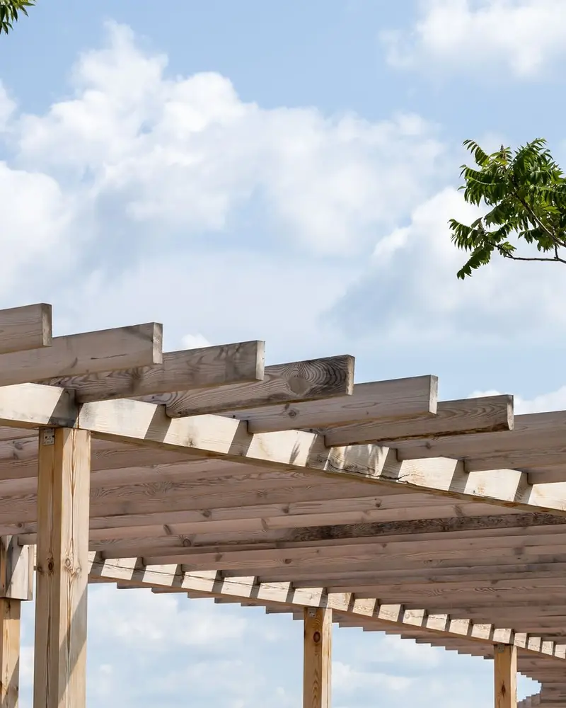 Lange Pergola aus unbehandeltem Holz mit Pfosten und Querbalken unter blauem Himmel
