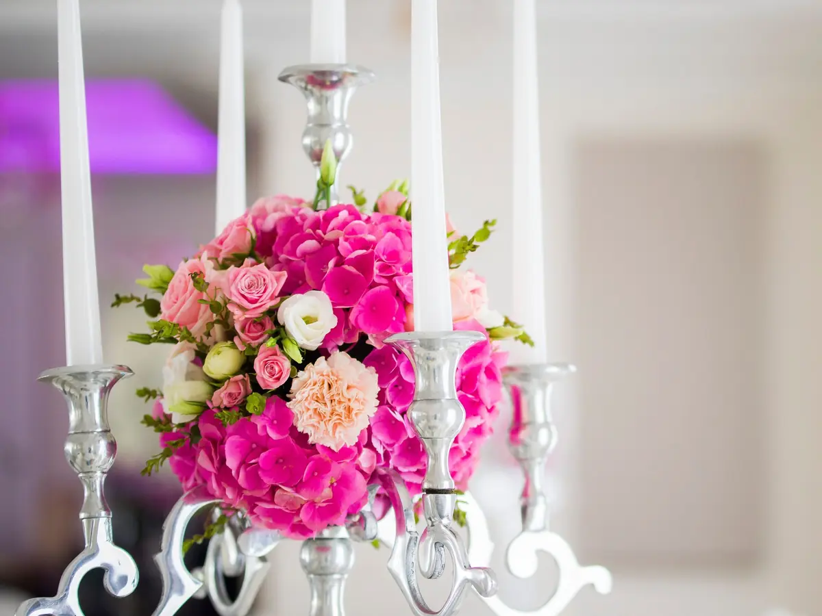 Silberner Kerzenleuchter mit weißen Kerzen und einer Kugel aus pinken Hortensien und Rosen