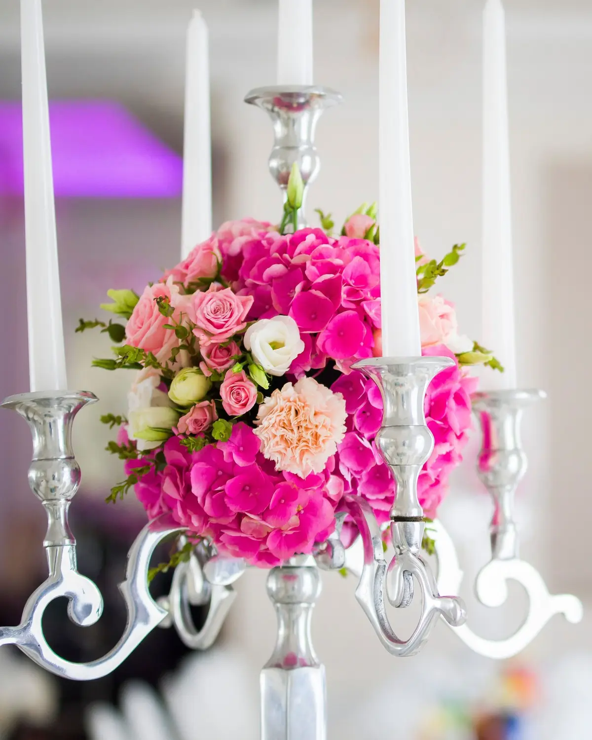 Silberner Kerzenleuchter mit weißen Kerzen und einer Kugel aus pinken Hortensien und Rosen