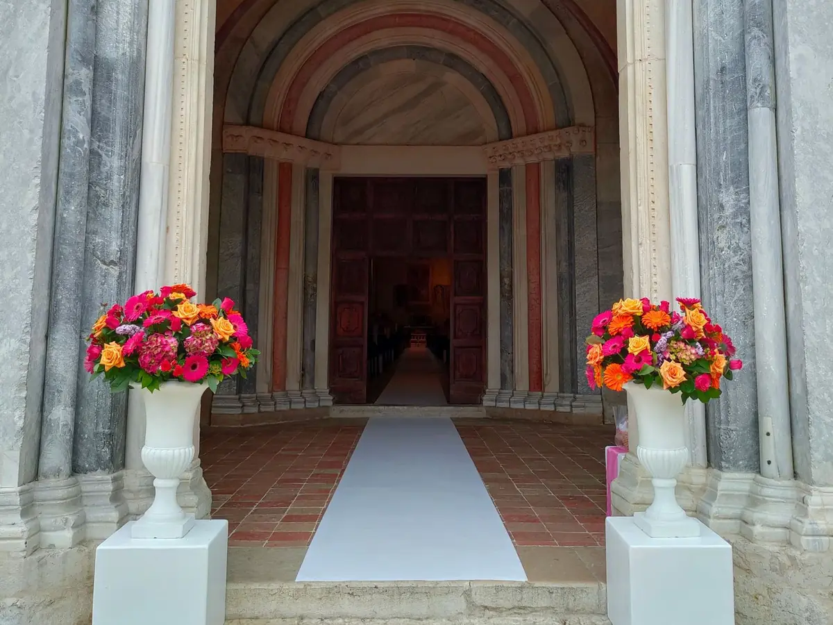 Romanisches Portal aus Marmor mit weißen Vasen voller Rosen und Gerbera und einem weißen Läufer zum Eingang