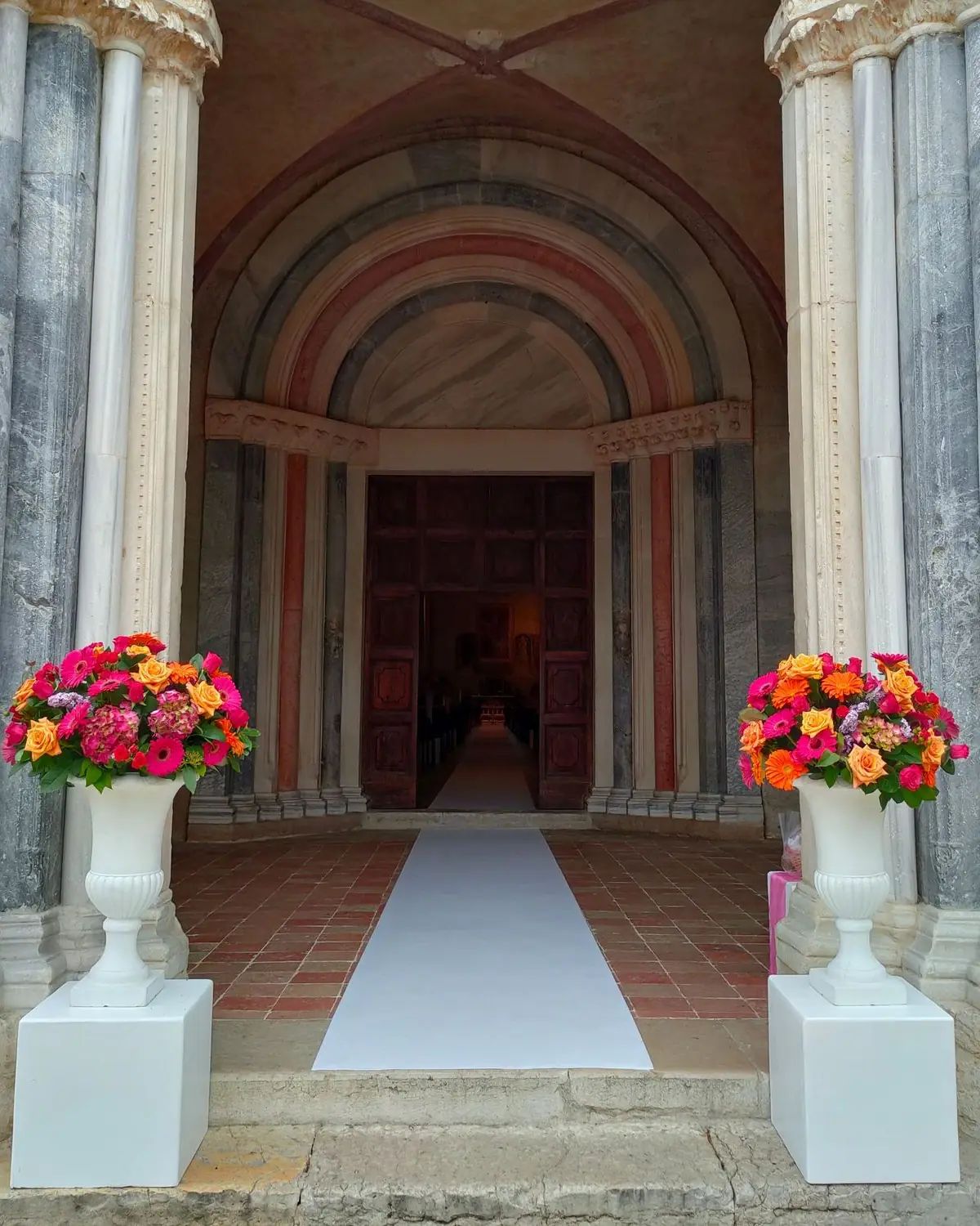 Romanisches Portal aus Marmor mit weißen Vasen voller Rosen und Gerbera und einem weißen Läufer zum Eingang