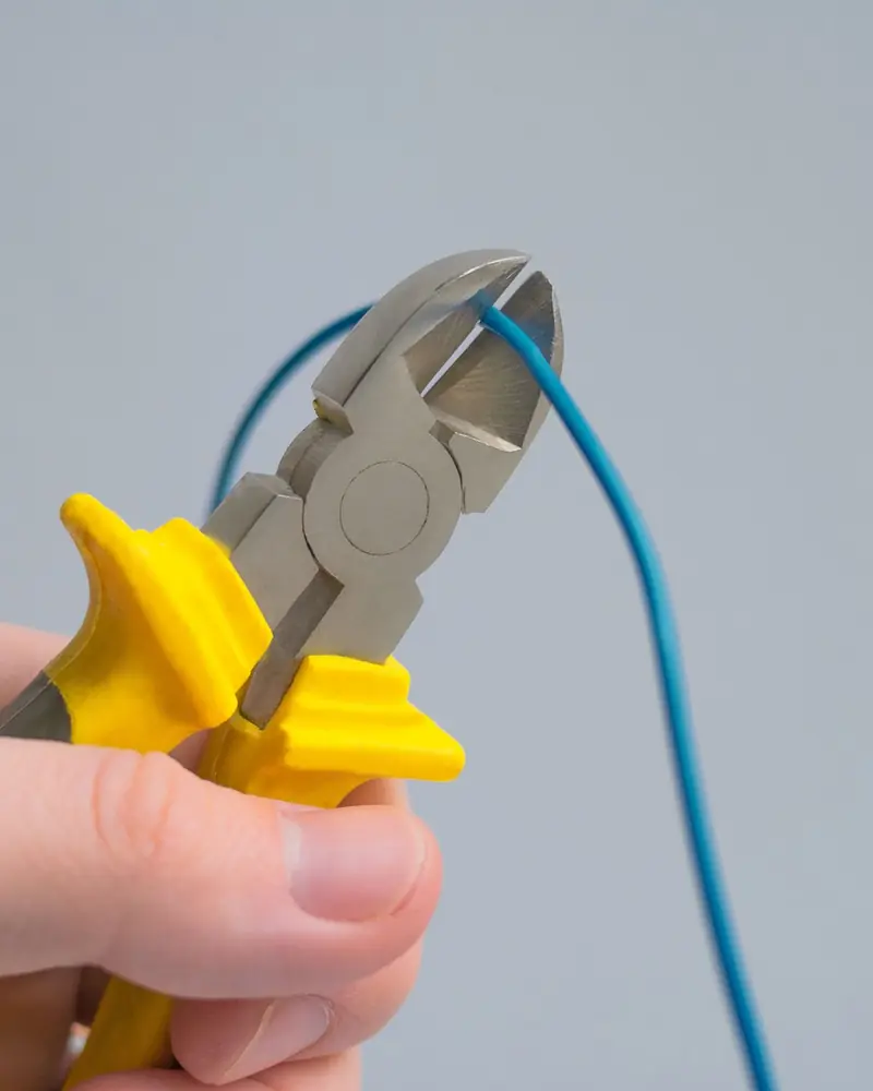 Hand mit Seitenschneider kneift ein blaues Kabel ab