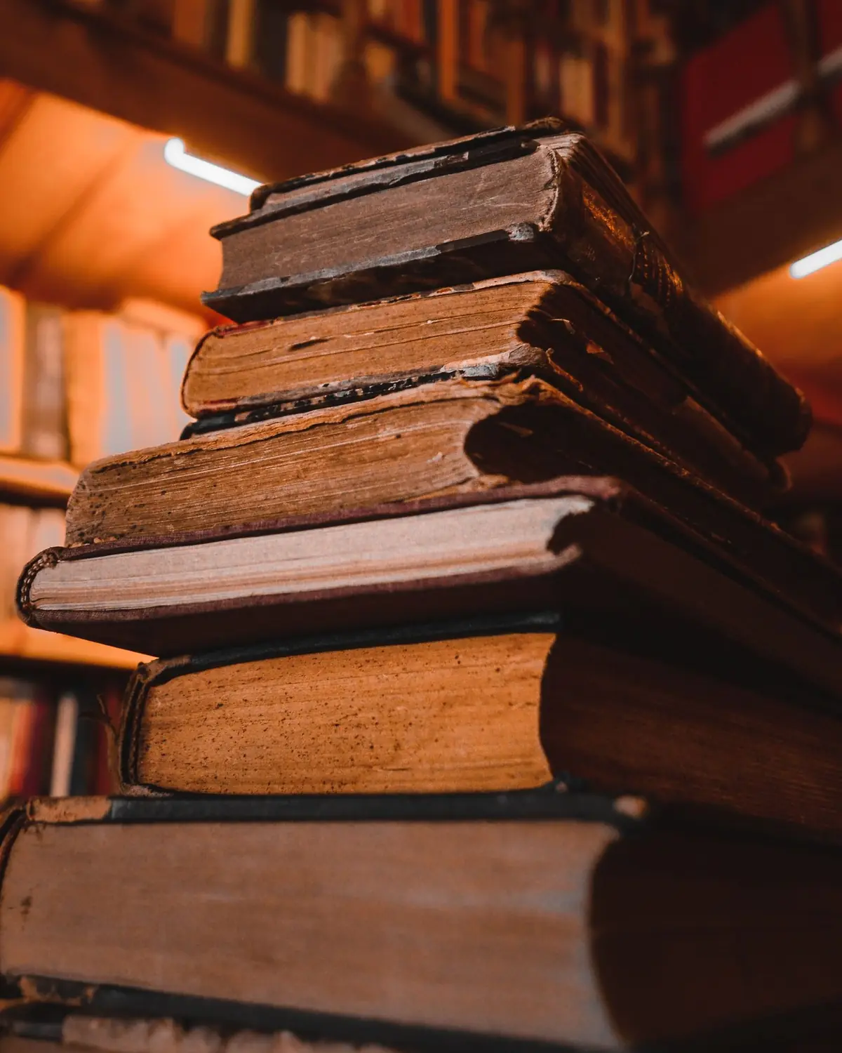 Stapel alter, abgegriffener Bücher mit Leinenrücken vor unscharfen Regalen im warmen Licht