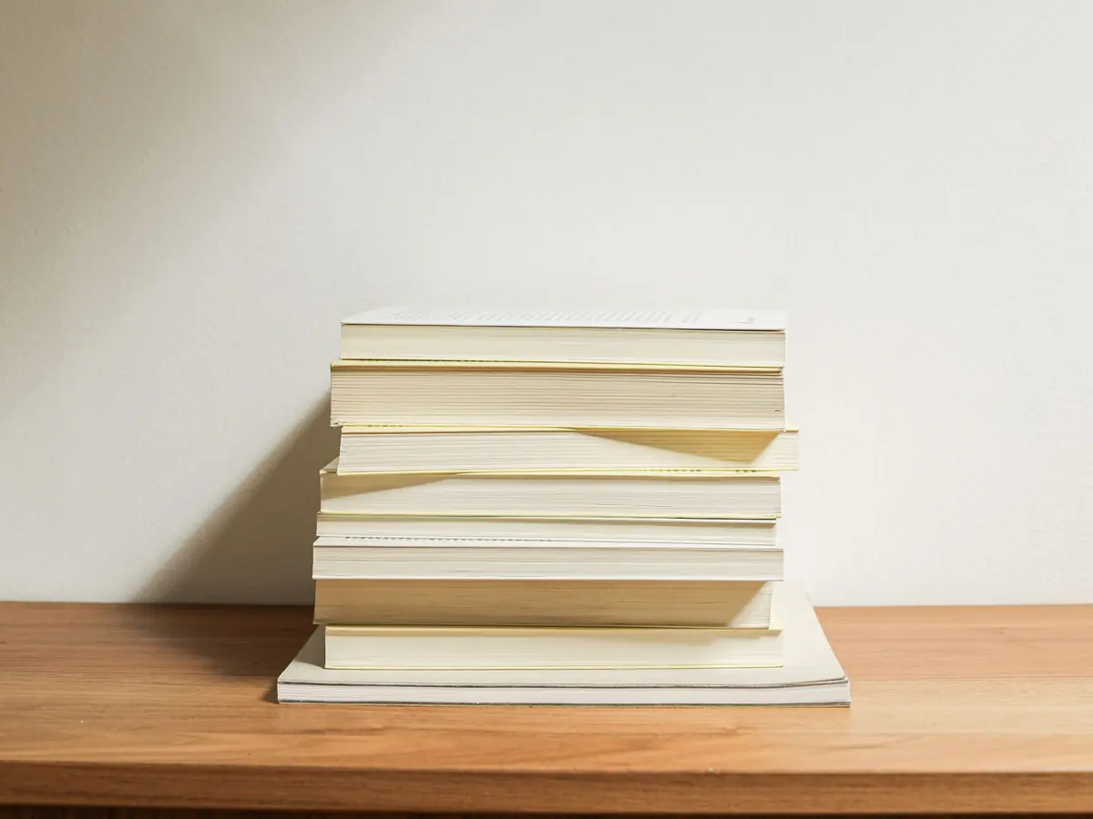 Stapel heller Taschenbücher ohne sichtbare Titel auf einem Holzbrett vor einer weißen Wand